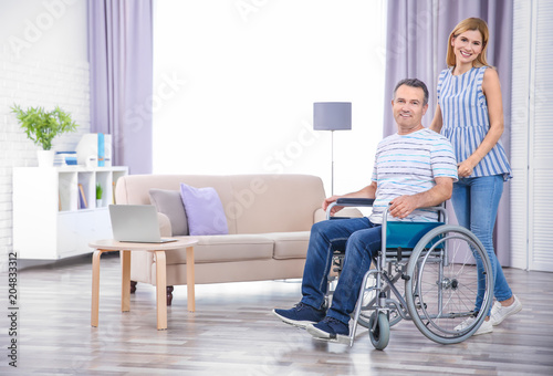 Young woman taking care of mature man in wheelchair indoors