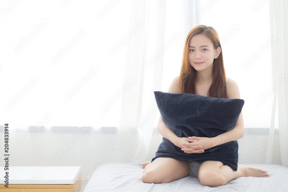 Portrait beautiful young asian woman sitting and smile hug pillow with the window at bedroom while wake up with sunrise at morning, lifestyle and relax concept. Portrait beautiful young asian woman sitting and smile hug pillow with the window at bedroom while wake up with sunrise at morning, lifestyle and relax concept.