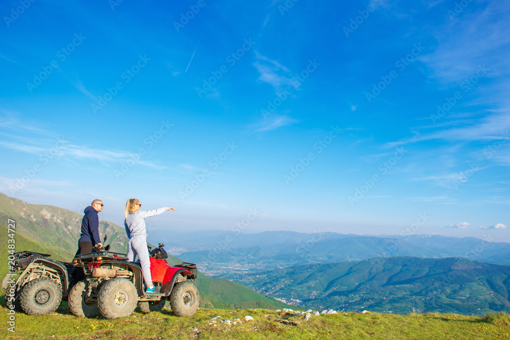 Beautiful couple is watching the sunset from the mountain sitting on atv quadbike Beautiful couple is watching the sunset from the mountain sitting on atv quadbike