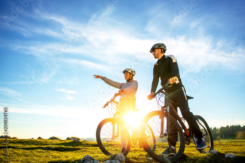 Biker couple with mountain bike pointing in distance at countryside