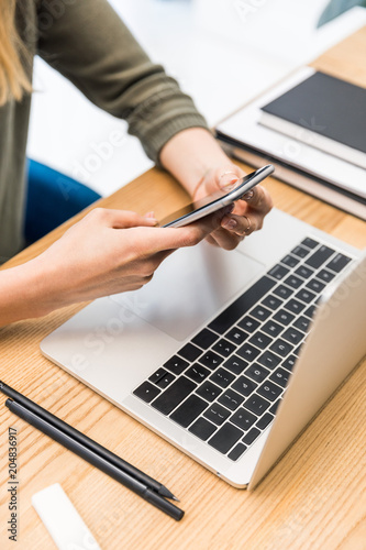 Valokuva cropped shot of businesswoman using smartphone at workplace with laptop