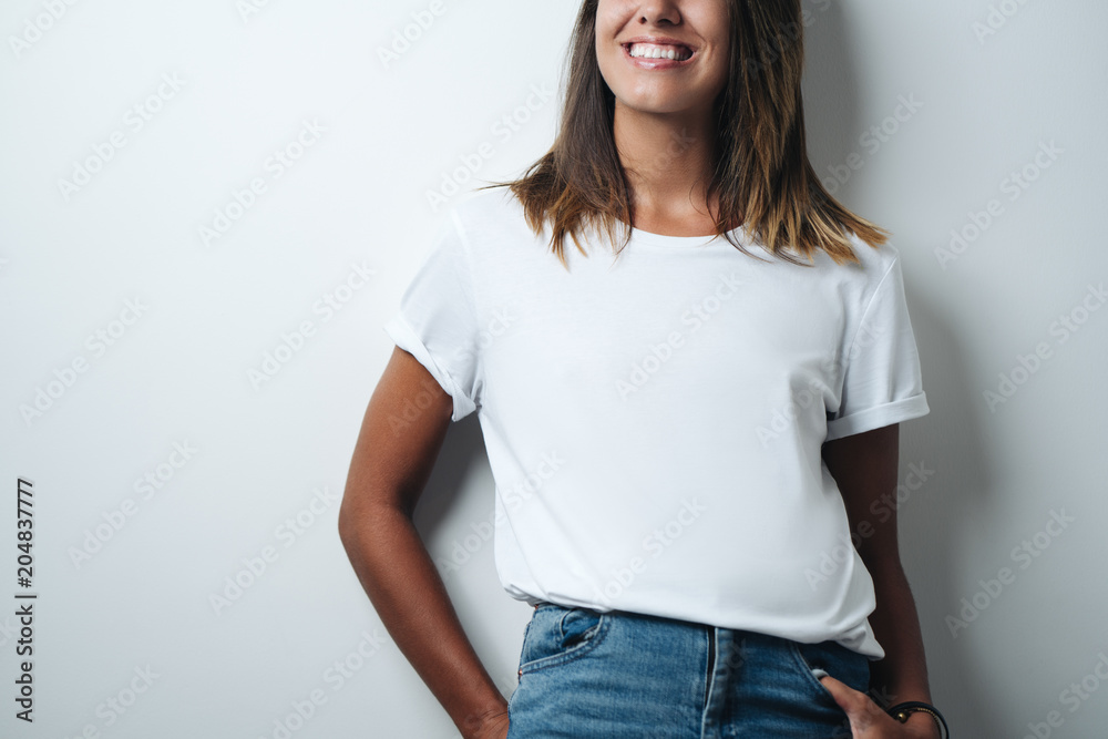 Obraz premium Smiling woman in white blank t-shirt, empty wall, horizontal studio close-up