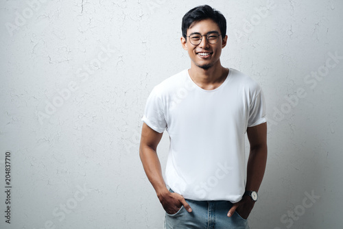 Smiling guy in glasses and white blank t-shirt, grunge wall, horizontal studio portrait