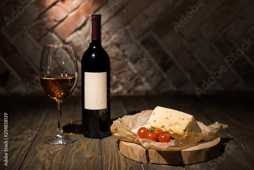 close up view of bottle and glass of wine with cheese and cherry tomatoes on baking paper on wooden decorative stump
