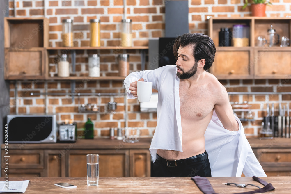 handsome loner businessman wearing shirt and holding cup of coffee at kitchen