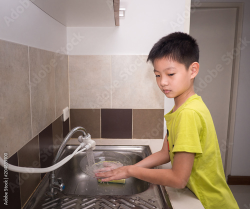 Adorable  kid boy washing dishes in domestic kitchen. Child having fun with helping his parents with housework.