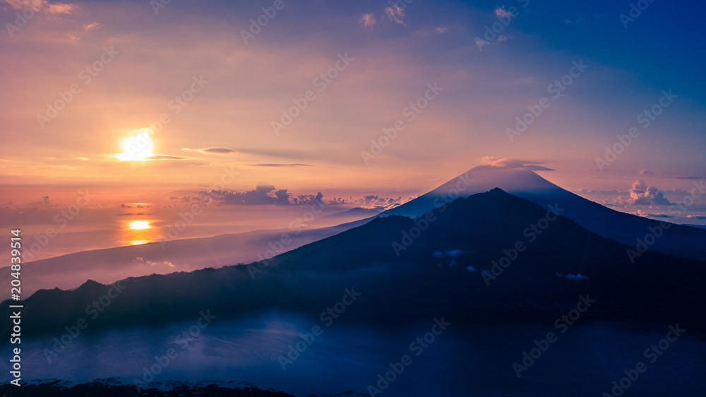 Sun rising and reflecting off a distant sea behind a mountain Sun rising and reflecting off a distant sea behind a mountain