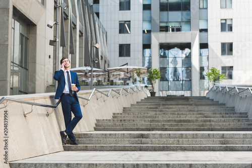 handsome young businessman in stylish suit with coffee to go talking by phone on stairs near business building © LIGHTFIELD STUDIOS