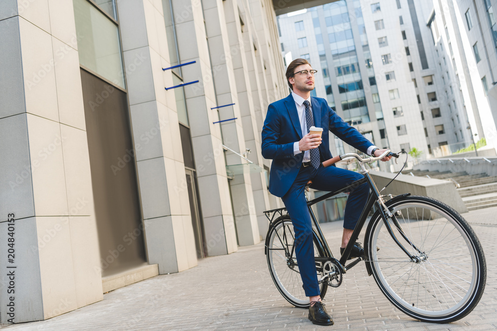 handsome young businessman in stylish suit with coffee to go sitting on vintage bicycle handsome young businessman in stylish suit with coffee to go sitting on vintage bicycle