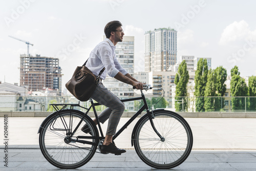 Fototapeta side view of young man in stylish clothes riding vintage bicycle on city street