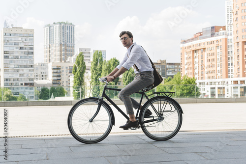 Fototapeta Naklejka Na Ścianę i Meble -  side view of attractive young man in stylish clothes riding vintage bicycle on city street