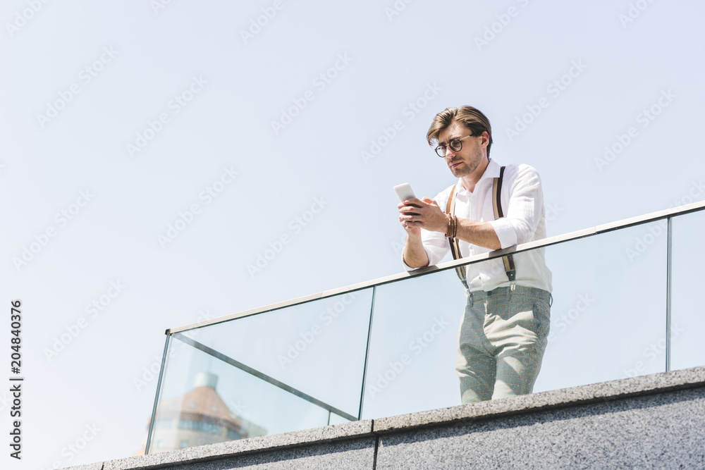 bottom view of handsome young man using smartphone on balcony bottom view of handsome young man using smartphone on balcony