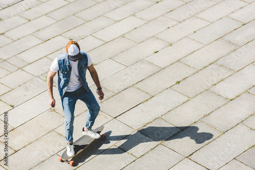high angle view of stylish young skater riding longboard by square