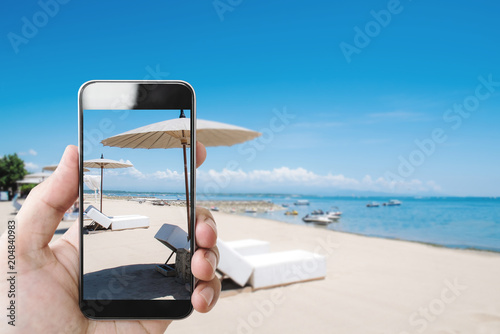 Fototapeta Naklejka Na Ścianę i Meble -  Summer holiday, hand holding mobile smartphone on the beach in summer