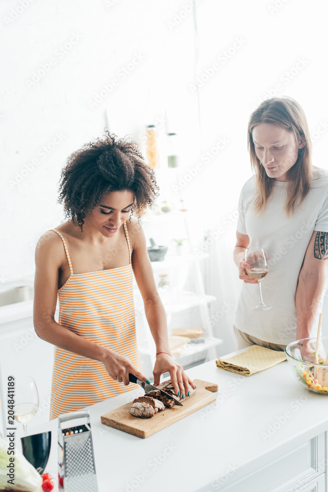 african american woman cutting bread and boyfriend standing near with wine glass african american woman cutting bread and boyfriend standing near with wine glass