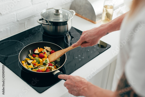 cropped shot of man cooking vegetables in frying pan on electric stove photo