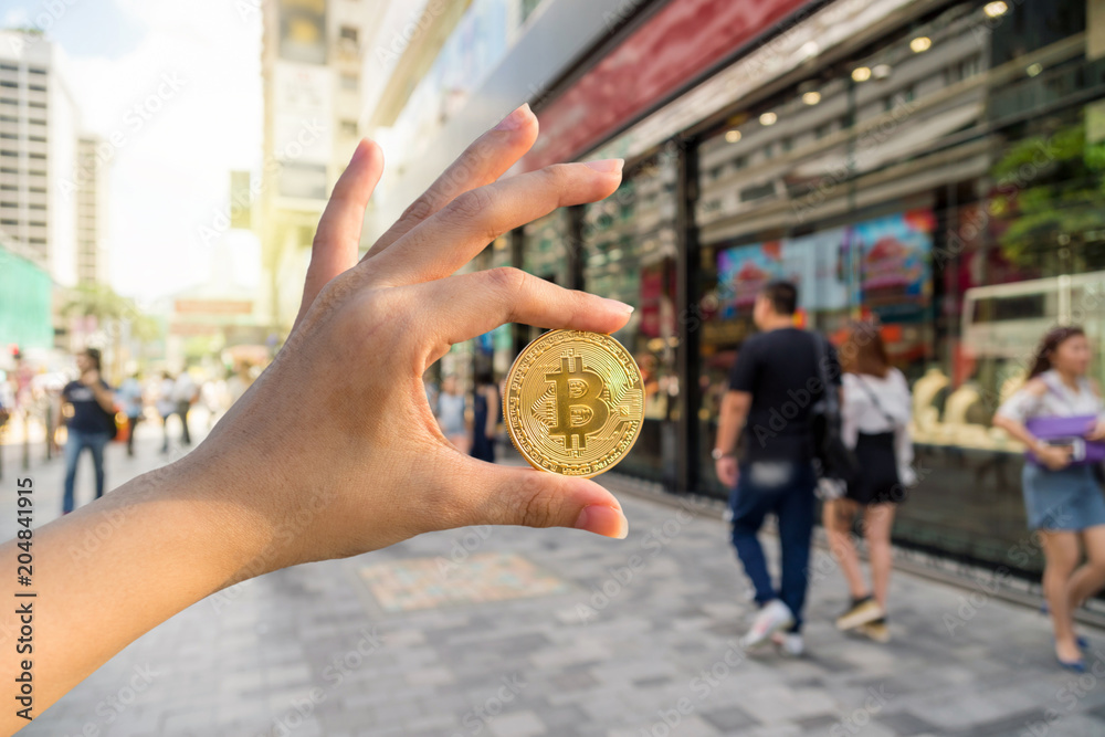 Closeup hand holding bitcoin over the Abstract blurred photo of shopping store in outdoor store mall with people walking streer, Block chain technology of Crypto concept, Business and future concept