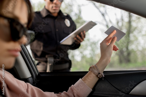 woman in sunglasses sitting in car and giving driver license to policeman