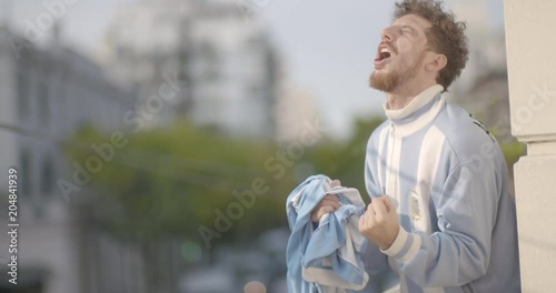 Happy Argentinian football supporter waving jersey while celebrating victory in balcony