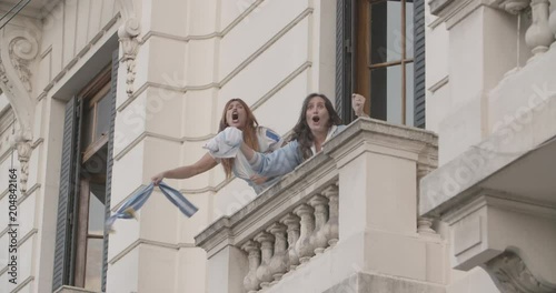 Happy Argentinian football supporters waving jersey and scarf while celebrating victory in balcony