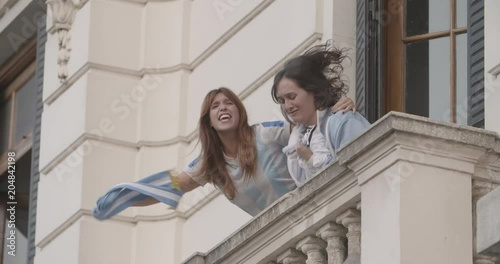 Happy Argentinian football supporters waving jersey and scarf while celebrating victory in balcony