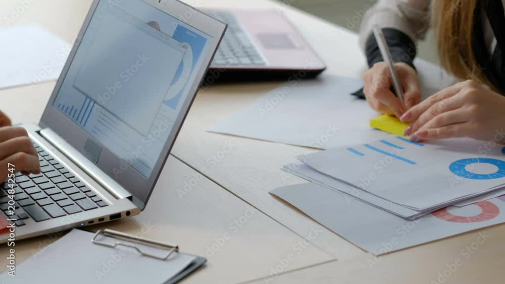 business data analysis paperwork. office workers casual workday routine. man and woman at their workplaces typing on laptop and writing a memo