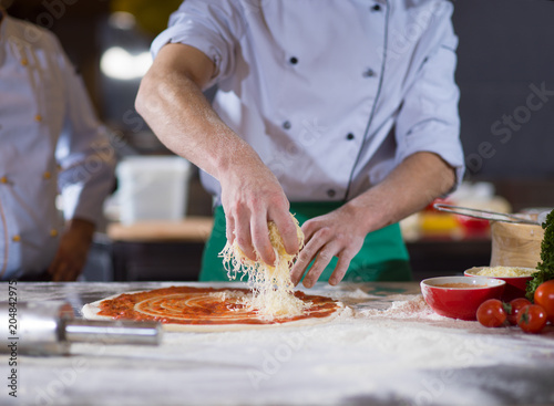 chef sprinkling cheese over fresh pizza dough