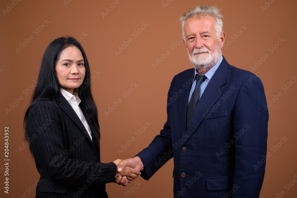 Mature multi-ethnic business couple against brown background Mature multi-ethnic business couple against brown background