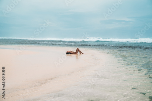 Beautiful girl in a swimsuit lies on the beach with white sand. Sexy model sunbathing on vacation near the ocean. Stunning landscape of the island with a tourist.