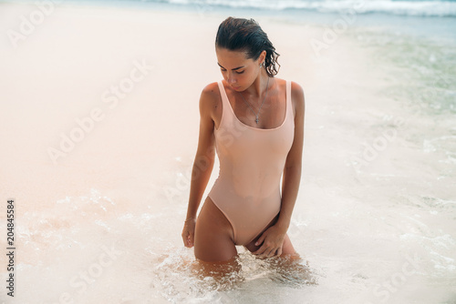 Charming girl in a bikini on summer vacation. A delightful woman with curly hair bathes in the ocean on a desert island in a swimsuit. Wet sexy tanned model body.