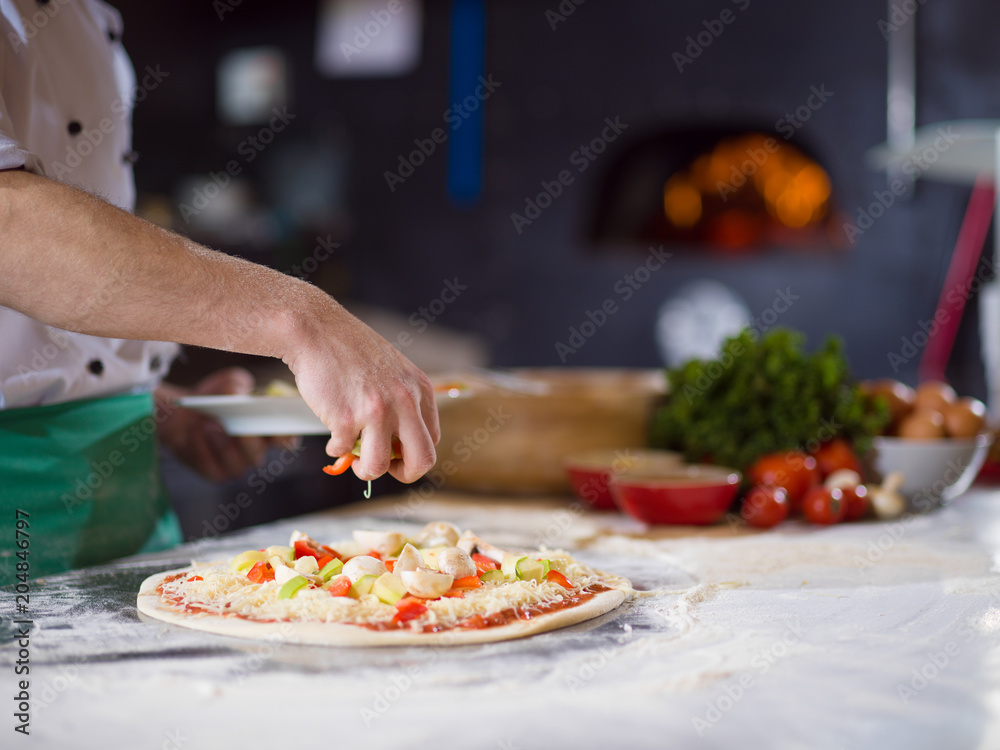chef putting fresh vegetables on pizza dough