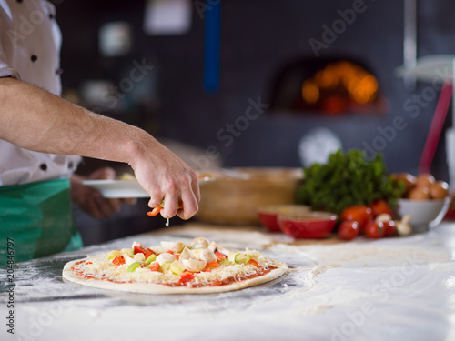 Fototapeta Naklejka Na Ścianę i Meble -  chef putting fresh vegetables on pizza dough