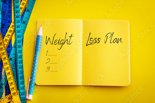 Weight loss and Diet control concept background. Colorful of Measuring tape on vibrant yellow color  background with blue book diary notepad and text as 