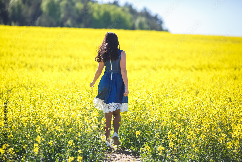 Girl in a blue dress leaves in a field of rapeseed. Follow me concept Girl in a blue dress leaves in a field of rapeseed. Follow me concept