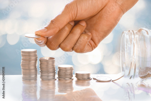 Save Woman's hand put or take money coins to / from stack of coins. Money, Financial, Business Growth or investment concept. With blue and white bokeh background.. photo