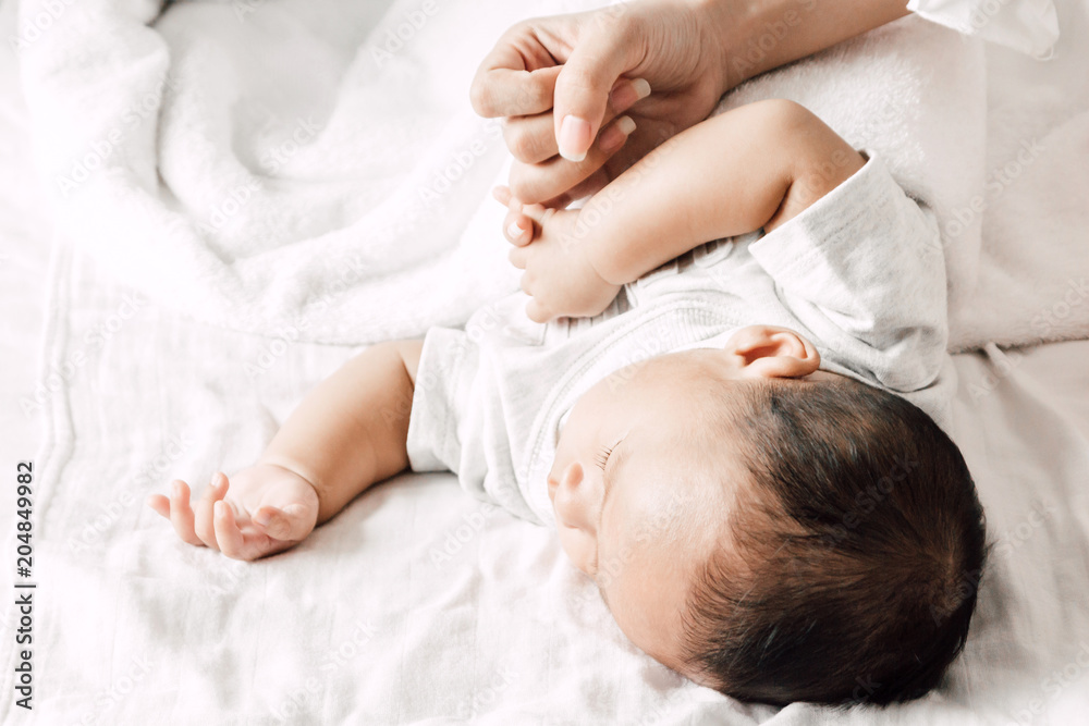 Mother holding sleeping baby hand on white bed.Love of family concept Mother holding sleeping baby hand on white bed.Love of family concept