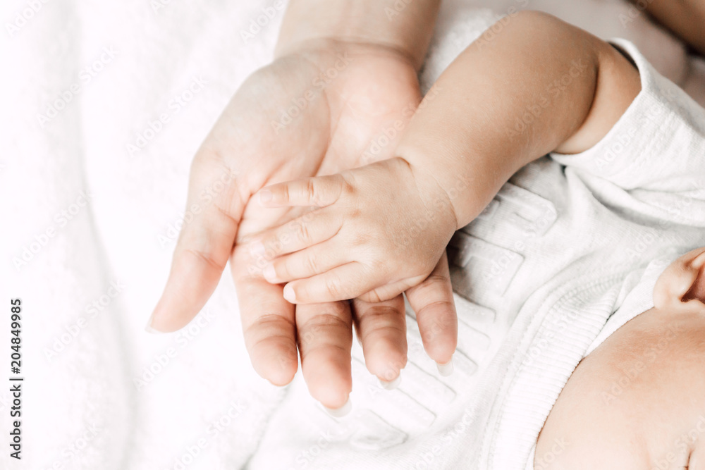 Mother holding sleeping baby hand on white bed.Love of family concept
