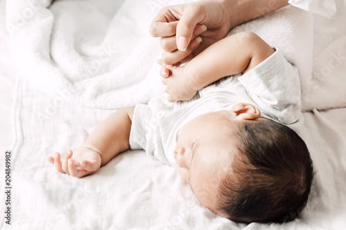 Mother holding sleeping baby hand on white bed.Love of family concept