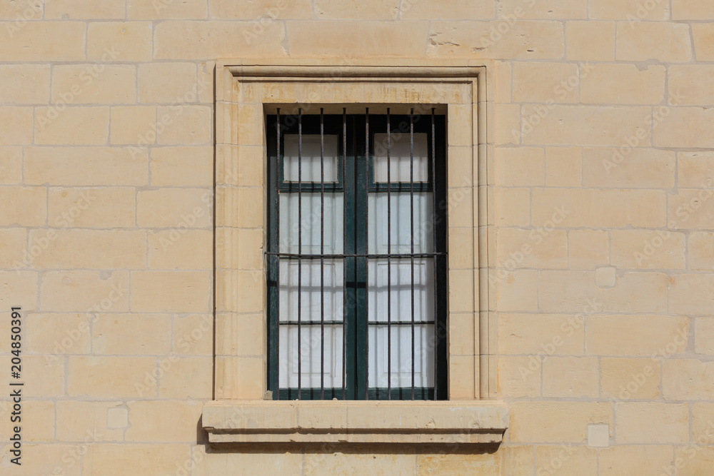 Malta, Valletta. Facade of yellow limestone house with closed window with metal bars, that provides safety. Close up view.