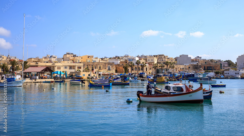 Marsaxlokk historic port full of boats in Malta. Blue sky and village background.