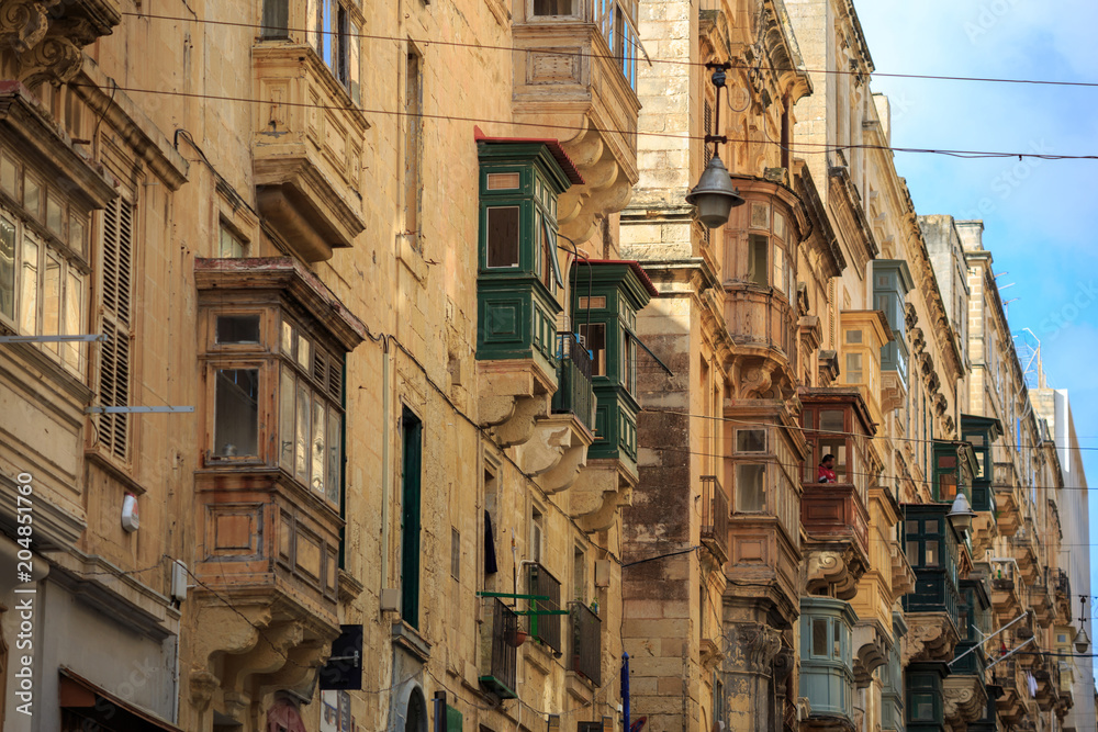 Malta, Valletta, traditional sandstone buildings with colorful wooden windows on balconies. Blue sky with clouds background. Close up view.