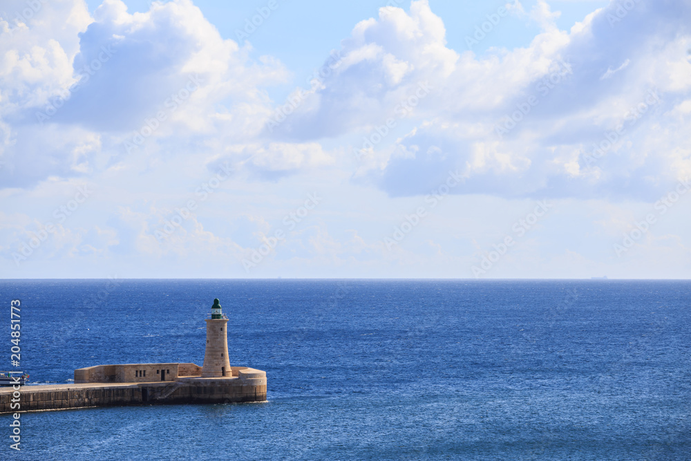 St. Elmo's lighthouse at Valletta, Malta. Breakwater of grand harbor between blue sea and sky background.