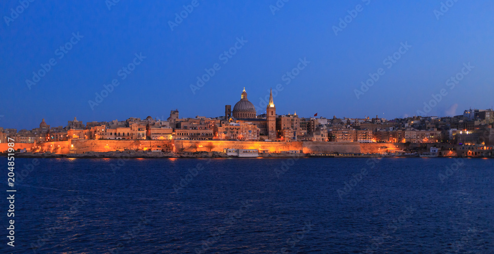 Valletta, Malta in the evening. Panoramic view of illuminated historic island and the dome of Carmelite Church and St Paul`s tower.