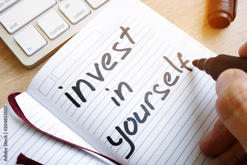 Man is writing invest in yourself in a note. - obrazy, fototapety, plakaty 