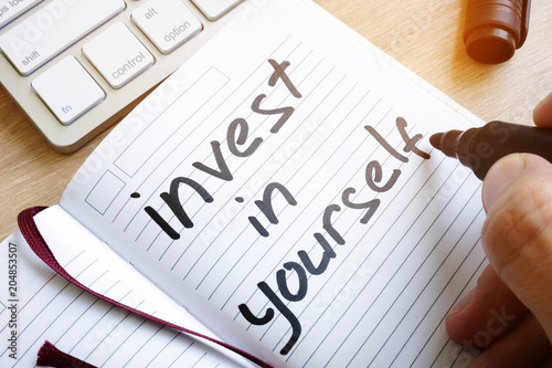 Man is writing invest in yourself in a note. photo