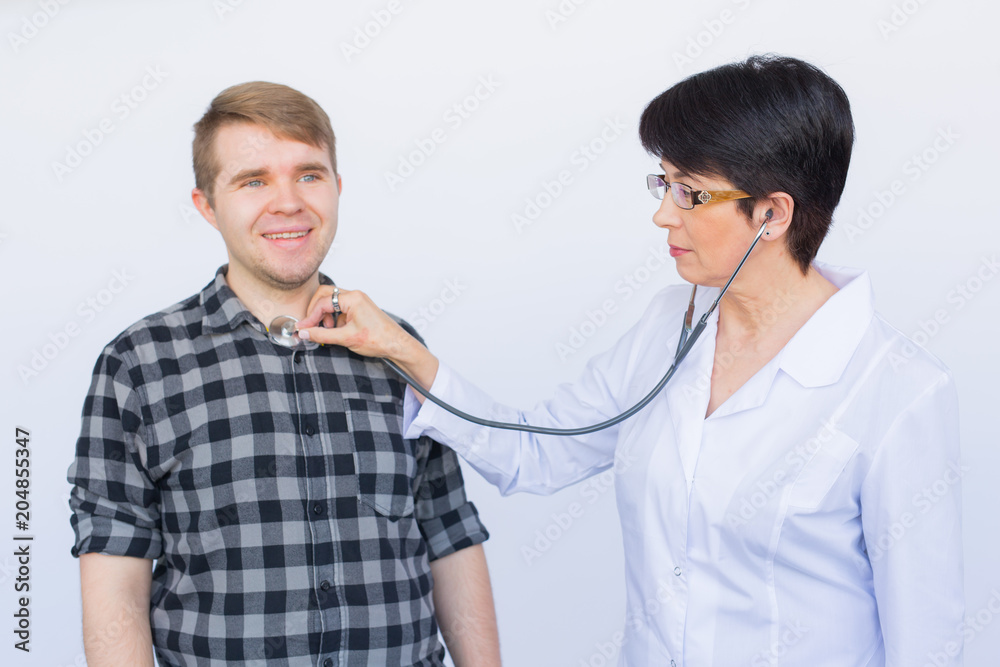 healthcare, medical exam, people and medicine concept - young man and doctor with stethoscope listening to heartbeat over white background healthcare, medical exam, people and medicine concept - young man and doctor with stethoscope listening to heartbeat over white background