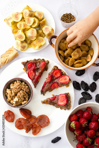 Sweets, dried fruits, chocolate cake with strawberries. Kid's hand taking sweets. Raw and vegan food.