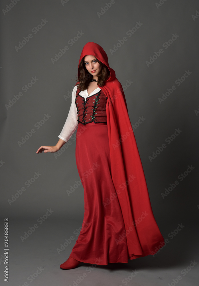 full length portrait of woman wearing red fantasy costume with cloak, standing pose on grey studio background.