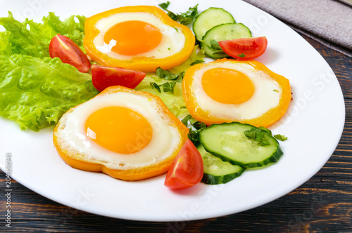 Fried egg in a circle of sweet pepper on a white plate with fresh vegetables on a wooden background. Delicious healthy breakfast. Proper nutrition.