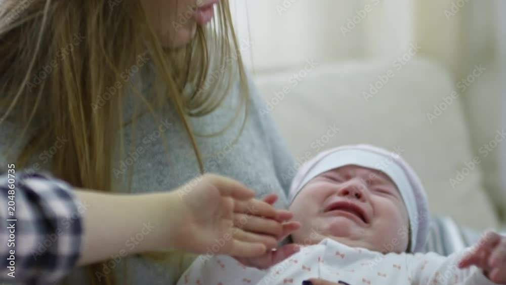 Tilt down of happy mother rocking crying baby as little girl and father caressing and soothing her Tilt down of happy mother rocking crying baby as little girl and father caressing and soothing her